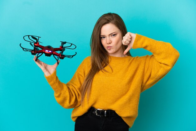 Tienermeisje met een drone over geïsoleerde blauwe achtergrond met duim omlaag met negatieve uitdrukking