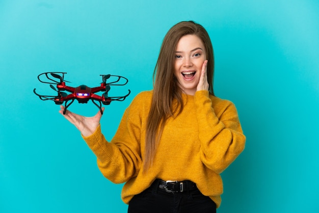 Tienermeisje met een drone over geïsoleerde blauwe achtergrond met verrassing en geschokte gezichtsuitdrukking