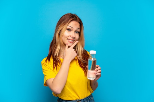 Tienermeisje met een fles water over geïsoleerde blauwe achtergrond gelukkig en glimlachend