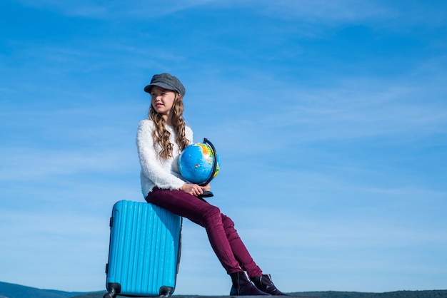 Tienermeisje met globe en reistas op de hemelachtergrond, kopieer ruimte, reizen.