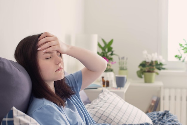 Tienermeisje met hoofdpijn op bed in witte kamer