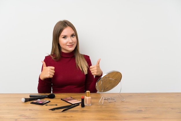 Foto tienermeisje met make-uppalet en schoonheidsmiddelen in lijst geven duimen op gebaar