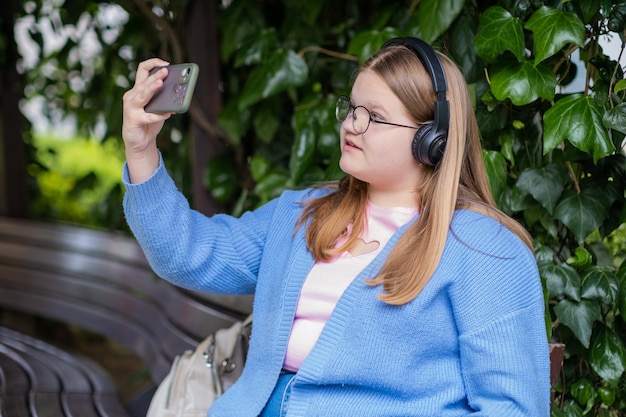 Tienermeisje met overgewicht in een koptelefoon die selfies maakt op de camera van een moderne smartphone