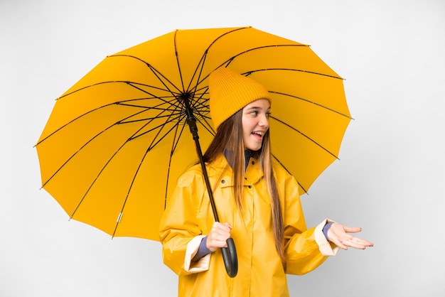 Tienermeisje met regenbestendige jas en paraplu over geïsoleerde witte achtergrond met verbaasde uitdrukking terwijl ze naar de zijkant kijkt