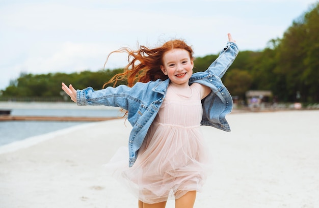 Tienermeisje met rood haar dat overdag springt en plezier heeft op het strand