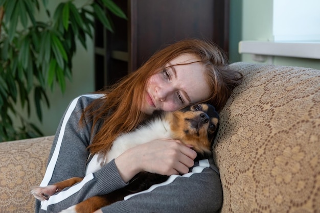 Tienermeisje met rood haar, generatie Z, huilend thuis in een omhelzing met een hond