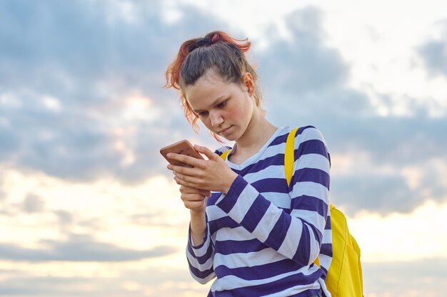 Tienermeisje met smartphone, de weideachtergrond van de hemelaard.