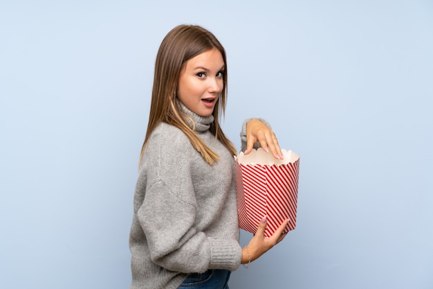 Tienermeisje met sweater over geïsoleerde blauwe etende popcorns