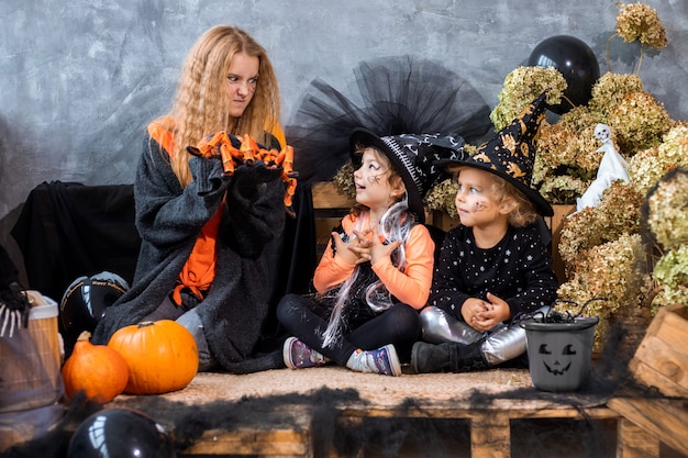Tienermeisje onder decor voor Halloween-vakantie met twee zussen van 4-5 jaar oud veel plezier op de achtergrond van zwarte en oranje versieringen, humorfoto