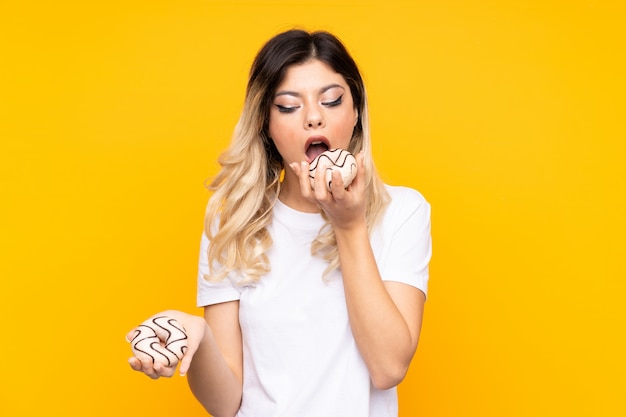 Tienermeisje op gele muur wordt geïsoleerd die een doughnut houden die