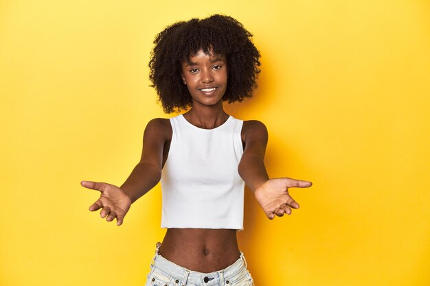 Tienermeisje op witte tanktop gele studioachtergrond die een welkome uitdrukking toont