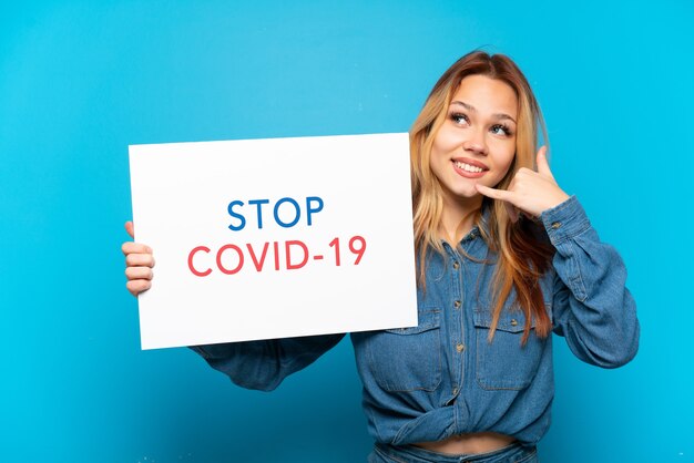 Tienermeisje over geïsoleerde blauwe achtergrond met een bordje met tekst Stop Covid 19 en telefoongebaar