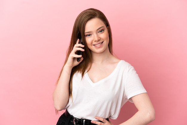 Tienermeisje over geïsoleerde roze achtergrond die een gesprek met de mobiele telefoon met iemand houdt