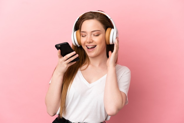 Tienermeisje over geïsoleerde roze achtergrond die muziek luistert met een mobiel en zingt