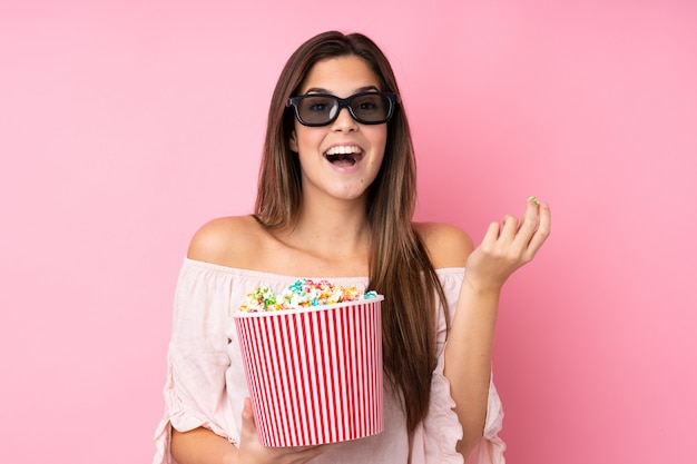 Tienermeisje over geïsoleerde roze muur met 3d glazen en holding een grote emmer popcorns