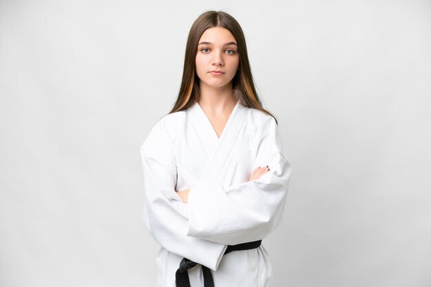 Tienermeisje over geïsoleerde witte achtergrond die karate doet en de armen gekruist houdt