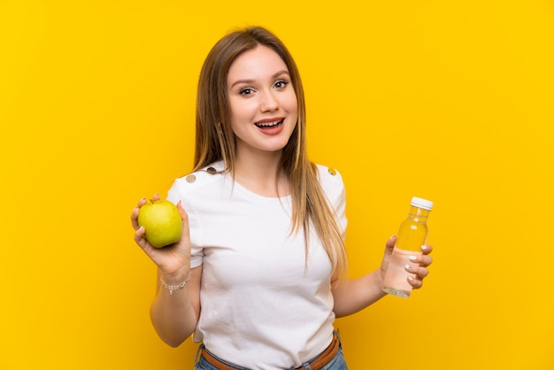 Tienermeisje over gele muur met een appel en een fles water