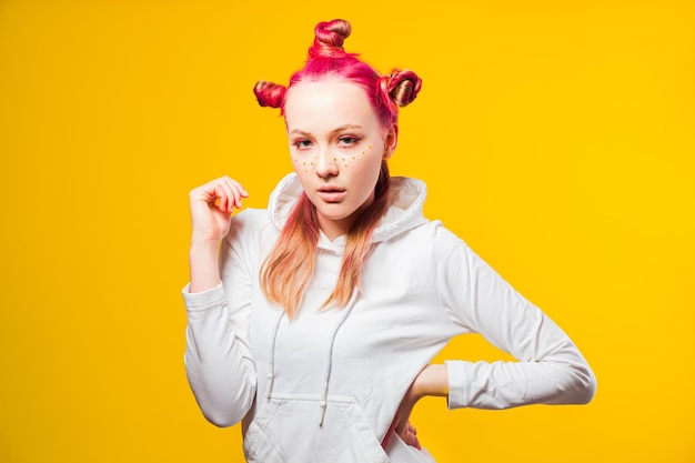 Tienermeisje poseren met provocerende blik Model met heldere trendy make-up is niet bang voor uitdagingen Meisje in witte hoodie op gele achtergrond