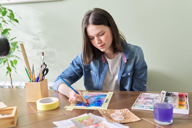 Tienermeisje schilderen met aquarellen, om thuis aan tafel te zitten. Kunst, onderwijs, creativiteit, tienerhobby's