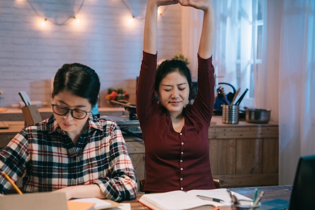 tienermeisje studente deed een dutje en werd wakker met het uitrekken van het lichaam terwijl haar beste vriendin zich concentreerde terwijl ze naast de tafel hardwerkend huiswerk maakte. twee vrouwen blijven 's avonds laat op om een zelfgemaakt project te maken.