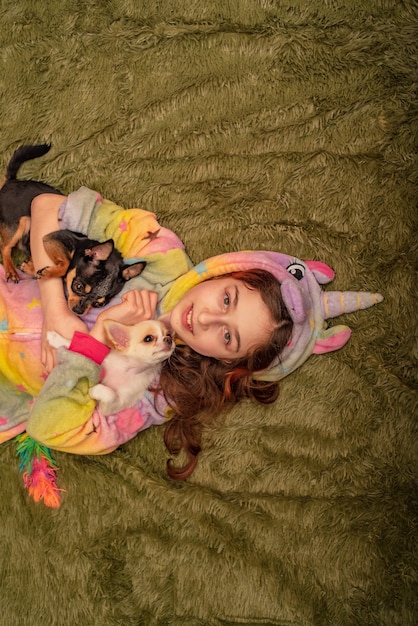 Tienermeisje thuis in pyjama op een groene plaid met een witte Chihuahua-puppy en een zwarte Chihuahua.