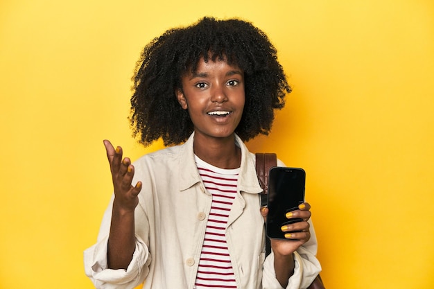 Tienermeisje toont een smartphone rugzak op gele achtergrond en krijgt een aangename verrassing