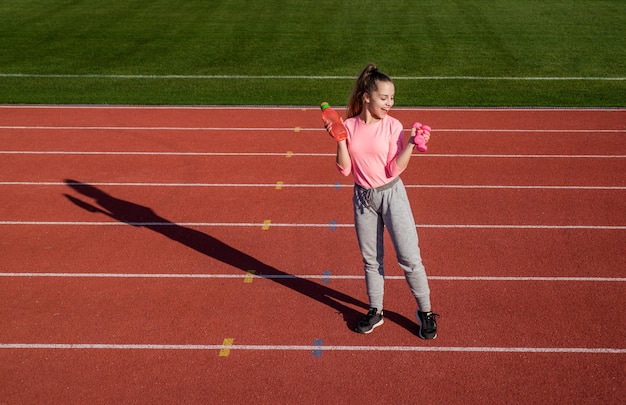 Tienermeisje training met halters en waterfles op outdoor stadion fitness