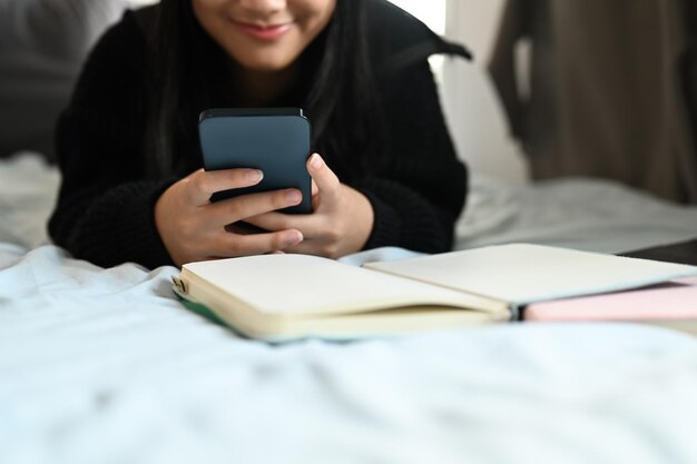 Tienermeisje typen tekstbericht chatten online op mobiele telefoon terwijl liggend op bed