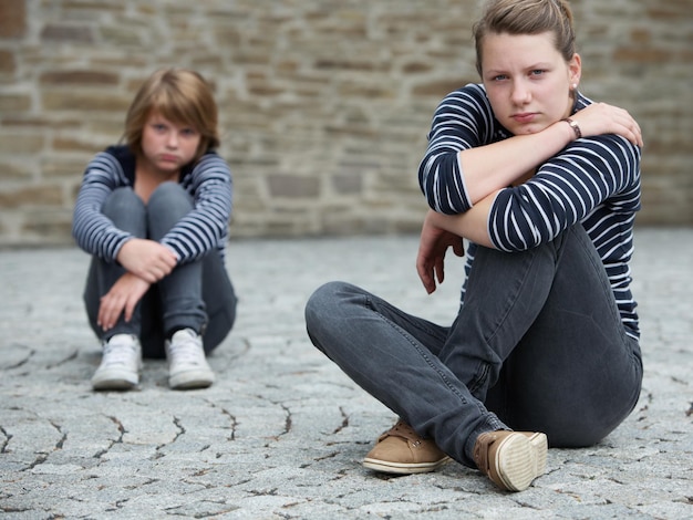 Tienermeisjes die op het terrein zitten, zich van elkaar afgekeerd