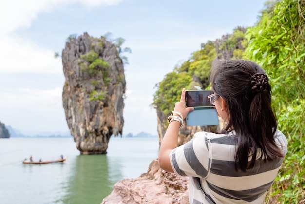 Tieners meisje toeristische schieten foto landmark een prachtig landschap op schilderachtig uitzicht door mobiele telefoon op Koh Tapu of James Bond Island in Ao Phang Nga Bay National Park, vrouw reizen natuur Azië in Thailand