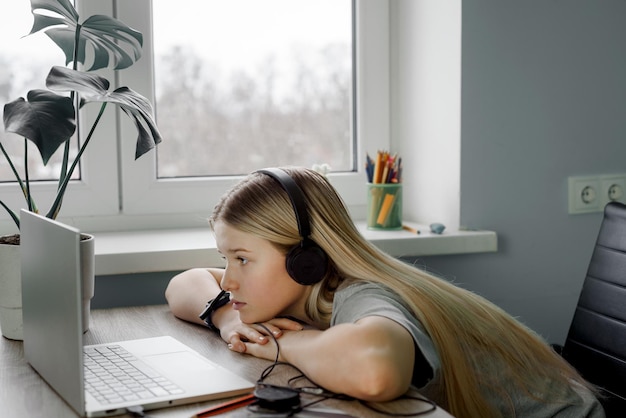Tieners met koptelefoon liggen op haar armen en kijken naar het computerscherm.