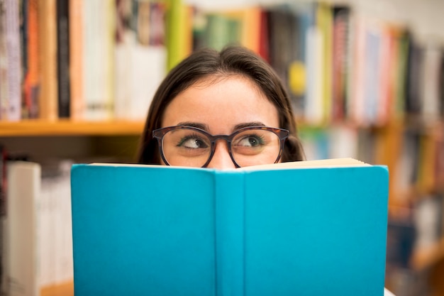 Foto tienerschoolmeisje die uit boek gluren