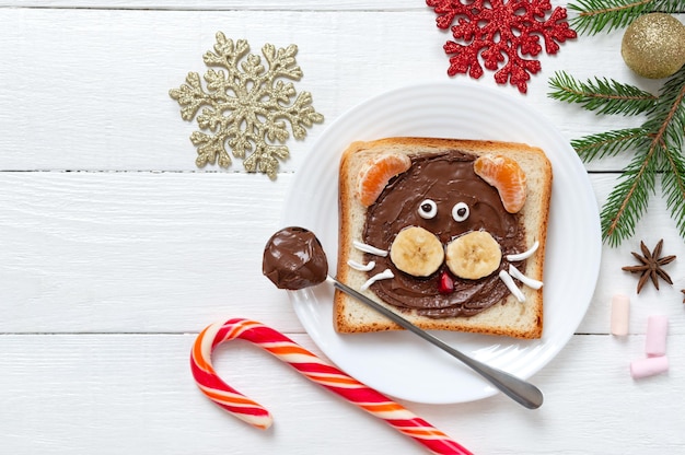 コピースペースのあるプレートにチョコレート、バナナ、タンジェリン、マシュマロを添えたタイガーヘッドサンドイッチ。新年、クリスマスの食事。子供のための健康食品のアイデア。上面図、フラットレイ