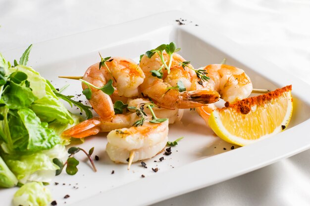 Tiger prawns on skewers with lemon and greens on a white dish