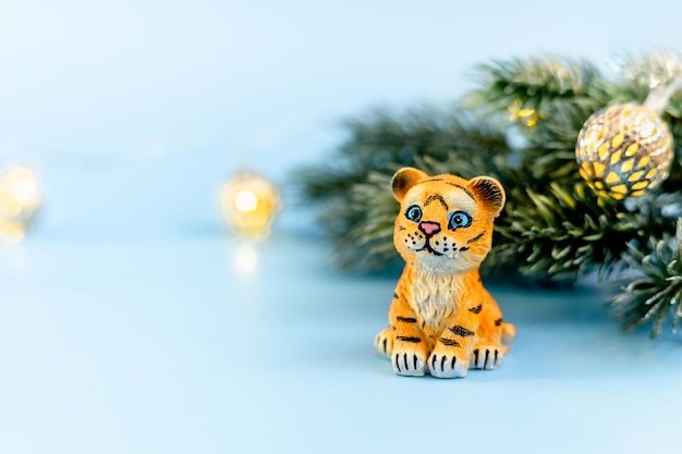 Tiger symbol of the Chinese new year 2022. Figurine of tiger with branches spruce tree on blue pastel background. Copy space.