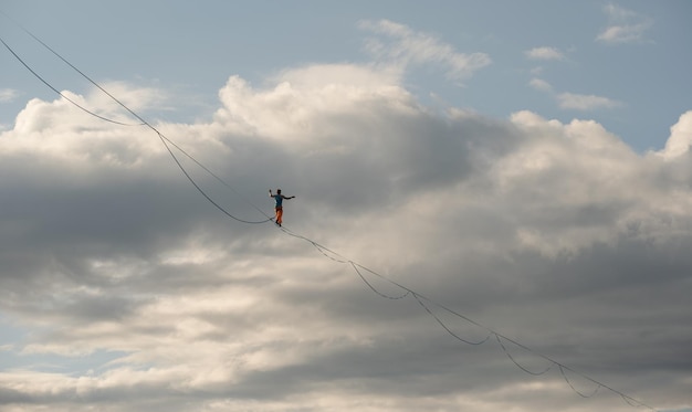 A tightrope walker walks along the highline Dramatic cloudy sky in background