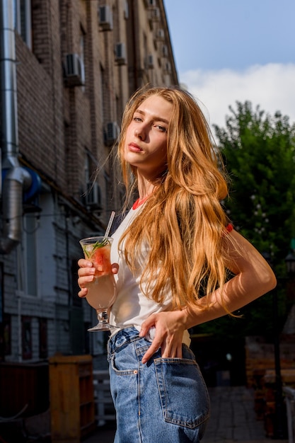 Tijd om een cocktail te drinken. Een heel mooie vrouw drinkt een cocktail. Natuurlijke blonde in t-shirt en spijkerbroek