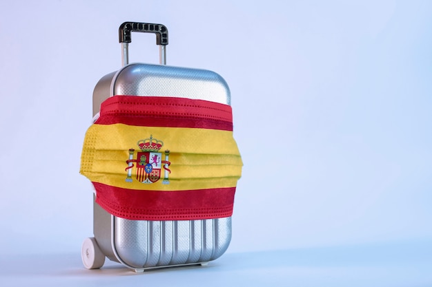 Tijd om te reizen. Het concept van veilige rust tijdens een pandemie Covid-19 Coronavirus. Koffer voor op reis met een medisch masker en Spaanse vlag.