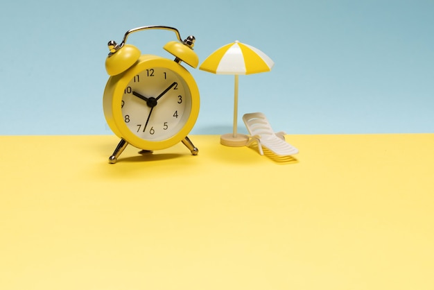 Tijd om te reizen. Ligstoel, gele paraplu en wekker op een gele, blauwe achtergrond.