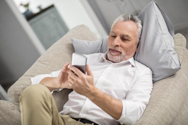 Tijd om te rusten. Opgetogen mannelijke persoon die positiviteit uitdrukt terwijl hij naar zijn telefoon kijkt en bericht leest