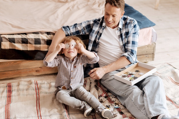 Tijd om te spelen. positief opgetogen man zittend op de vloer terwijl hij naar zijn zoon keek en hem ging omhelzen