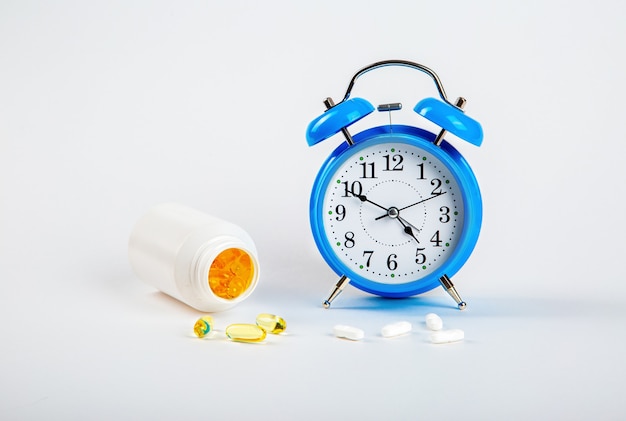 Tijd om uw pillen in te nemen. Een wekker op een witte muur toont de tijd van het innemen van medicijnen, en daarnaast - medische pillen.