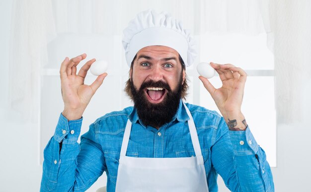 Tijd voor het eten van eieren hoe ei te koken gelukkig bakken concept van huishouding volwassen bebaarde man dragen chef-kok hoed mannelijke kok bereiden van voedsel in huis keuken brutale hipster in schort koken maaltijd