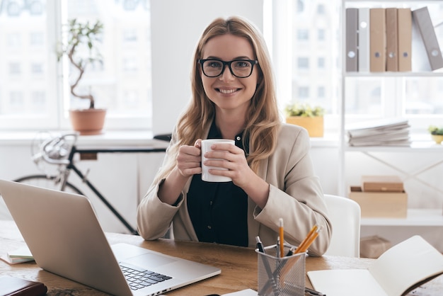 tijd voor koffiepauze. jonge vrouw in slimme vrijetijdskleding met een kopje koffie