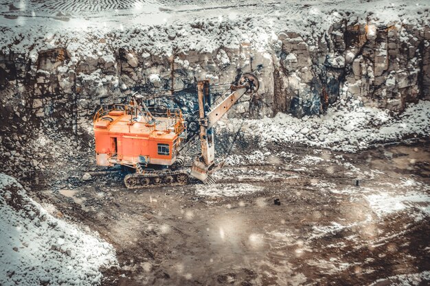 Tijdens een sneeuwval grote enorme gele graafmachine in een granietgroeve in de winter. enorme laadschop staat op een granieten vloer bezaaid met sneeuw in zijn carrière op een winterdag