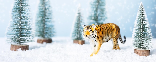Tijgersymbool van het Chinese nieuwe jaar 2022. Beeldje van tijger, dennenboom en sneeuw op blauwe achtergrond. Kerst wenskaart. Banner, kopieer ruimte.