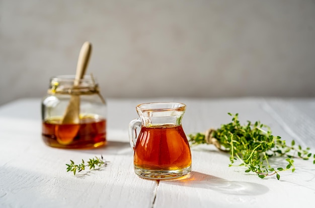 Tijmhoning in kleine kruik en pot kleine tijmtak op witte houten tafel met grijze achtergrond