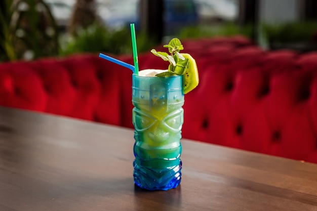 A tiki style cocktail in a colorful blue glass, kiwi and mint garnish at the bar