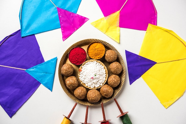 Til Gul OR Sweet Sesame Laddu with Miniature Fikri and Kite model with haldi Kumkum and sugar Crystals for Makar Sankranti Festival over Moody Background、Selective Focus