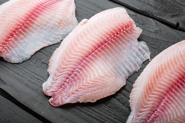 Tilapia visfilet vlees bezuinigingen, op zwarte houten tafel